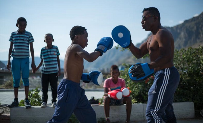 A boxing trainer in El Valle del Chota works with a youth to improve the boy's hook while other boxers in training look on.