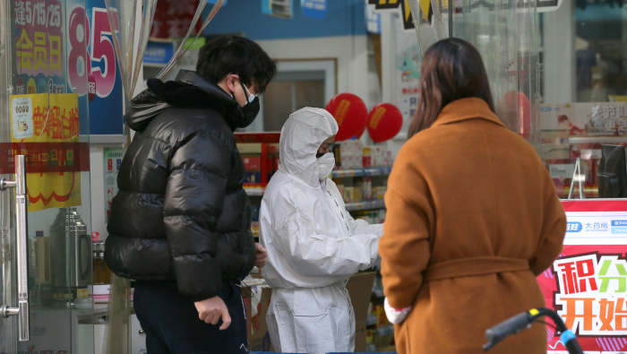 Un trabajador con traje protector atiende a los clientes en una farmacia en Wuhan, China.