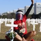 Una activista porta una mascarilla y careta mientras permanece sentada entre cruces colocadas simbolizando a las personas que han fallecido por la Covid-19 en Brasil.